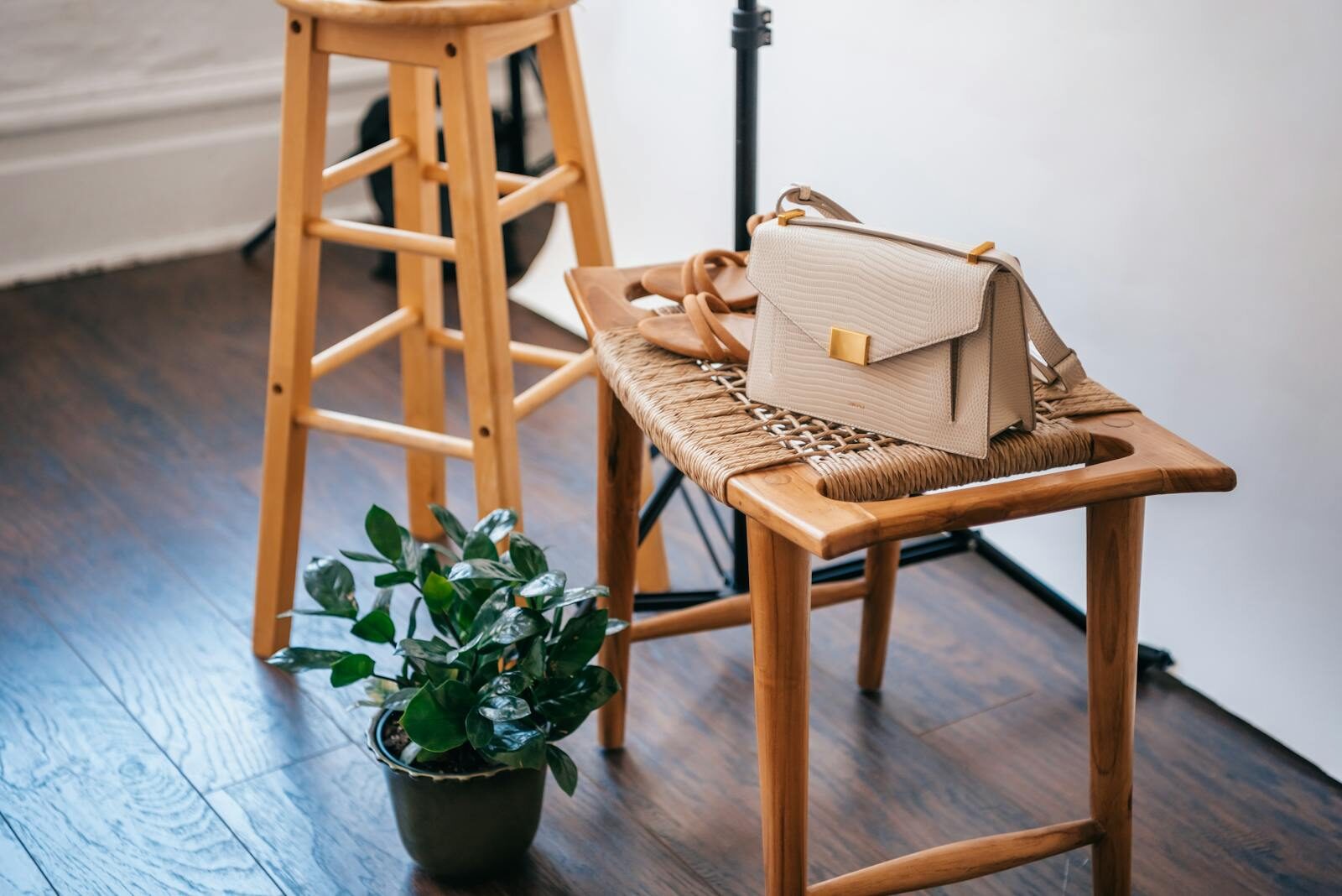 Stylish beige handbag on woven wooden stool with a potted plant in a cozy indoor setting.